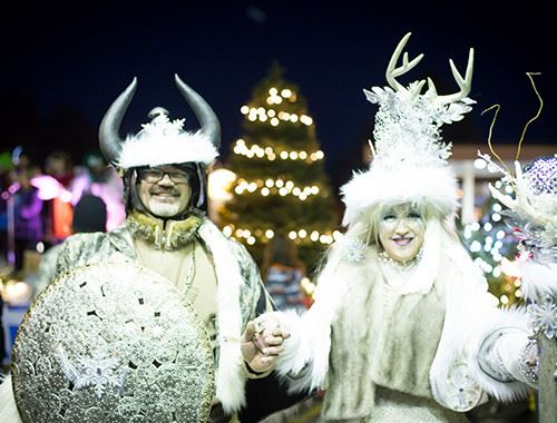 Two people in white costumes with a brightly lit tree in the background